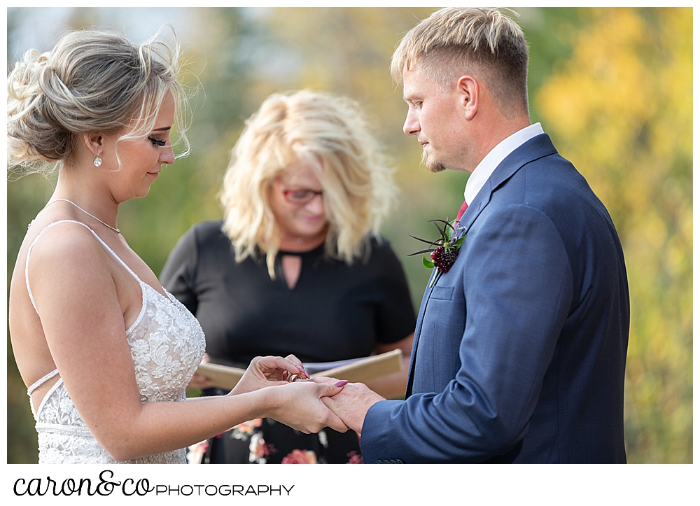 a bride puts a wedding band on her groom's finger during their outdoor Rangeley Maine wedding ceremony