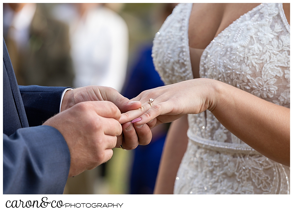 a groom puts the bride's wedding band on her finger during their Rangely Maine wedding ceremony