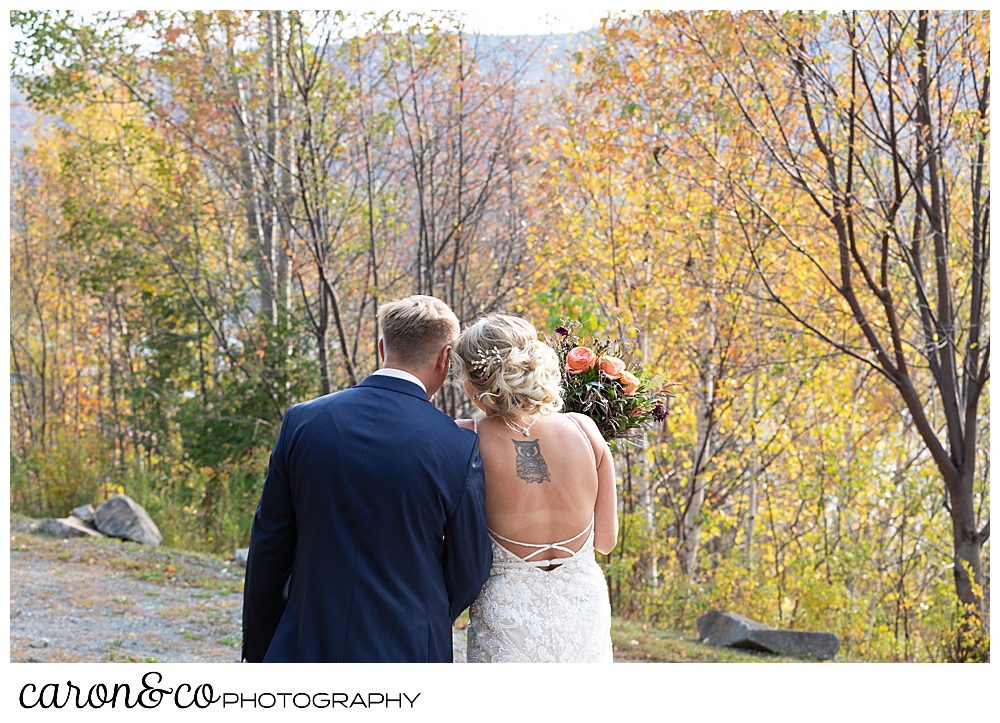 a bride and groom stand with their backs to the camera, their heads together, during their Rangeley Maine wedding day