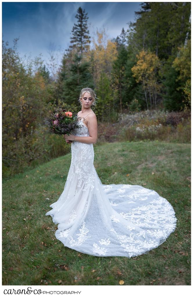 full length bridal portrait of a bride in a white dress, with a train, standing outside during her Rangeley Maine wedding