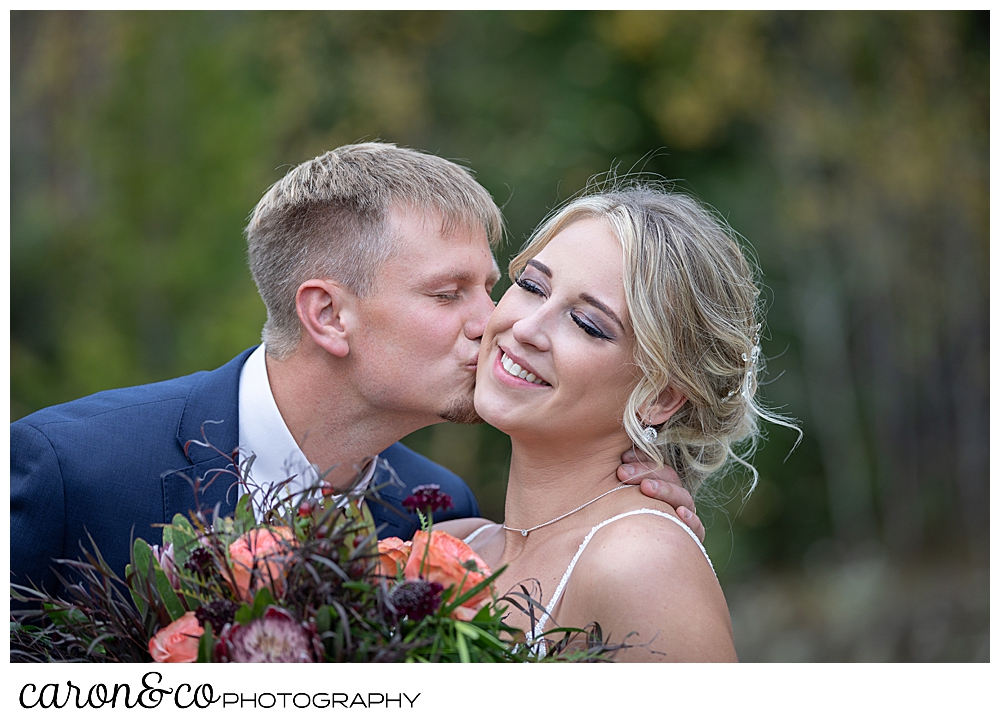 a bride smiles with her eye closed, as her groom kisses her cheek