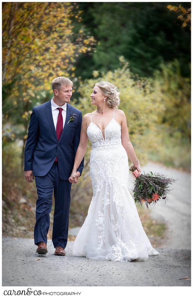 a bride and groom walking hand in hand in the fall foliage at a Rangeley Maine wedding