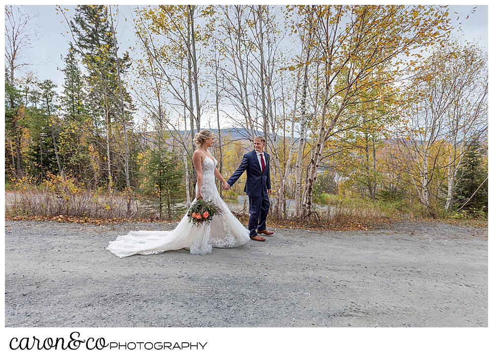 a bride and groom walk past, hand in hand in a Rangeley Maine wedding fall foliage