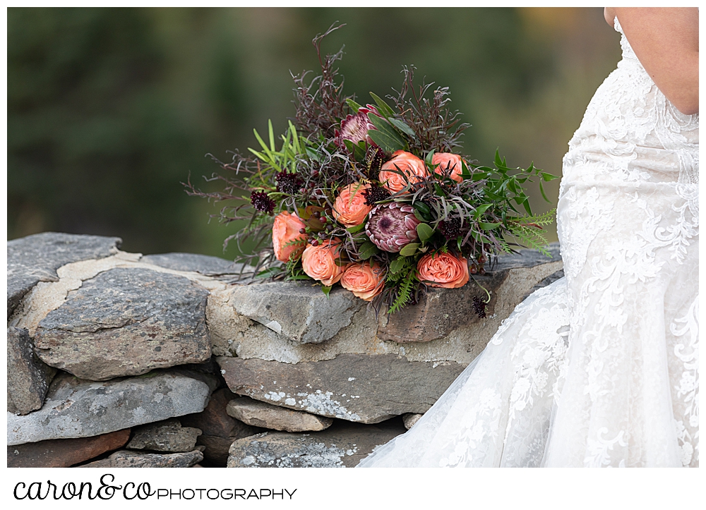 a bride's bouquet of peach roses and greenery, sits on a stone wall