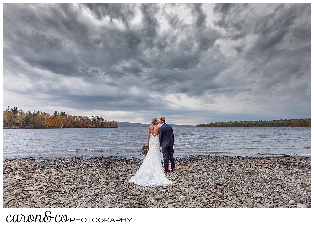 a bride and groom kiss on the shore of Rangeley Lake, 