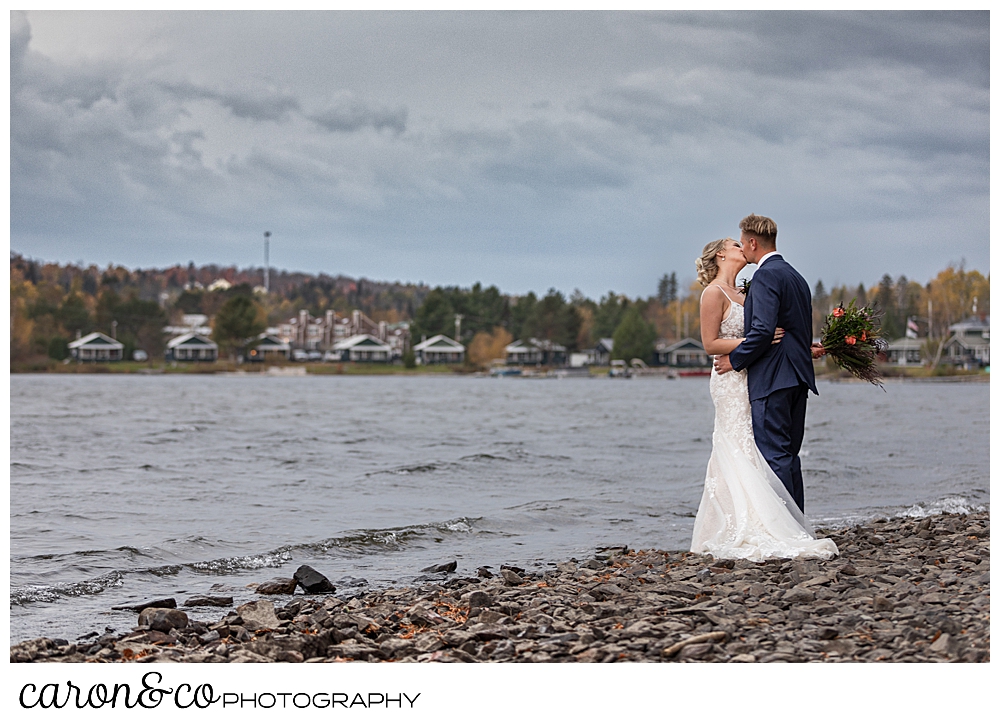 a bride and groom kiss while standing on the shore of Rangeley Lake, Rangeley Maine