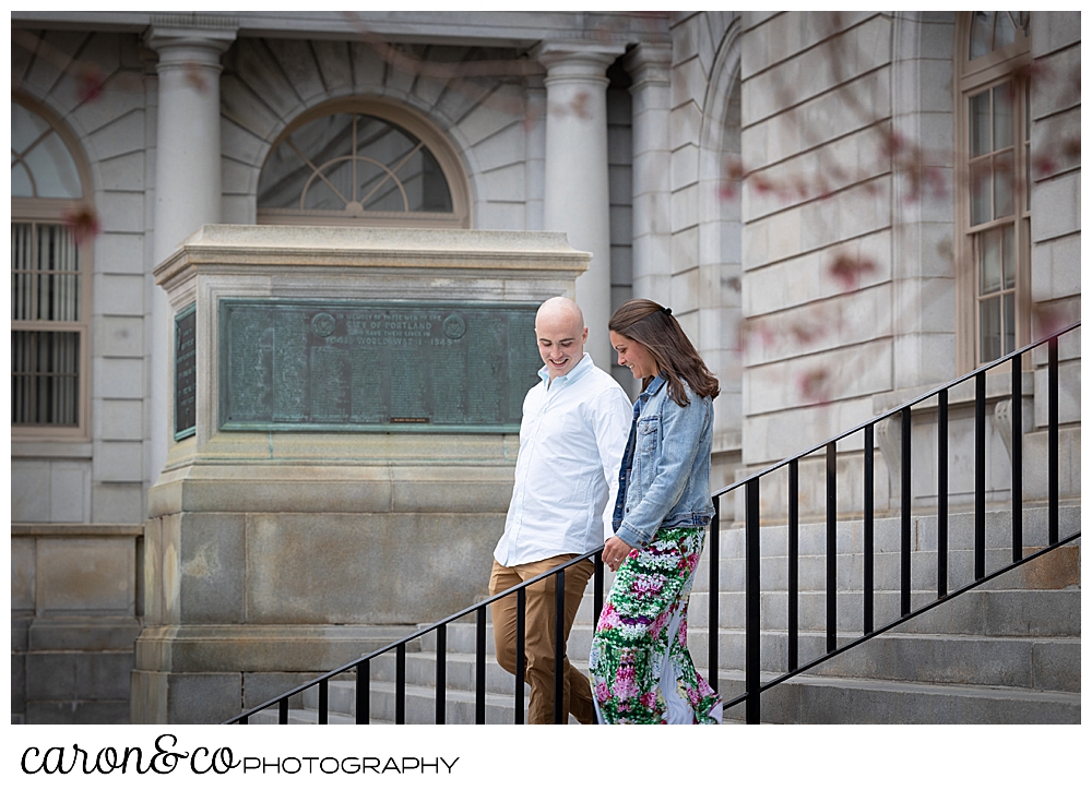 man and woman holding hands walking down the steps of the Portland Maine City Hall, during a Portland Maine spring engagement photo session