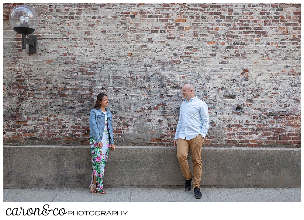 a man and woman standing in front of a brick wall in Portland, Maine, during a Portland Maine engagement session