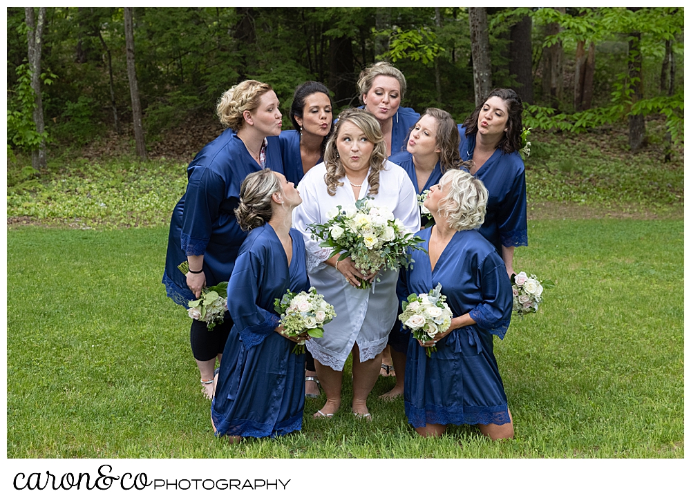 bride in a white robe, surrounded by bridesmaids in blue robes, blowing kisses