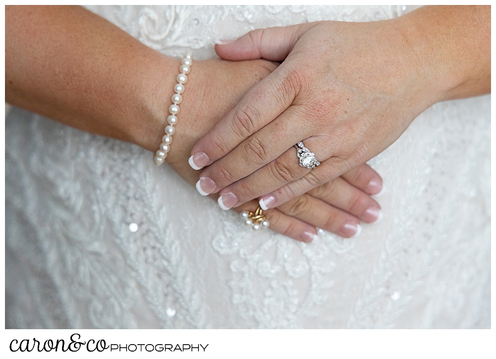 a bride's hands, clasped in front of her, she's wearing a diamond engagement ring, and a pearl bracelet