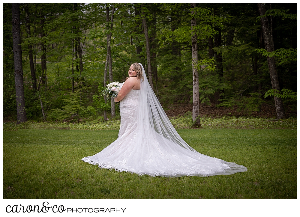 a full length portrait of a bride wearing a white strapless bridal gown, and a chapel length veil, stands in her back yard