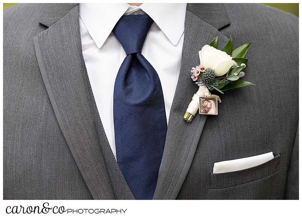 groom details, a gray suit, a white pocket square and shirt, a navy tie, and a white and green boutonniere