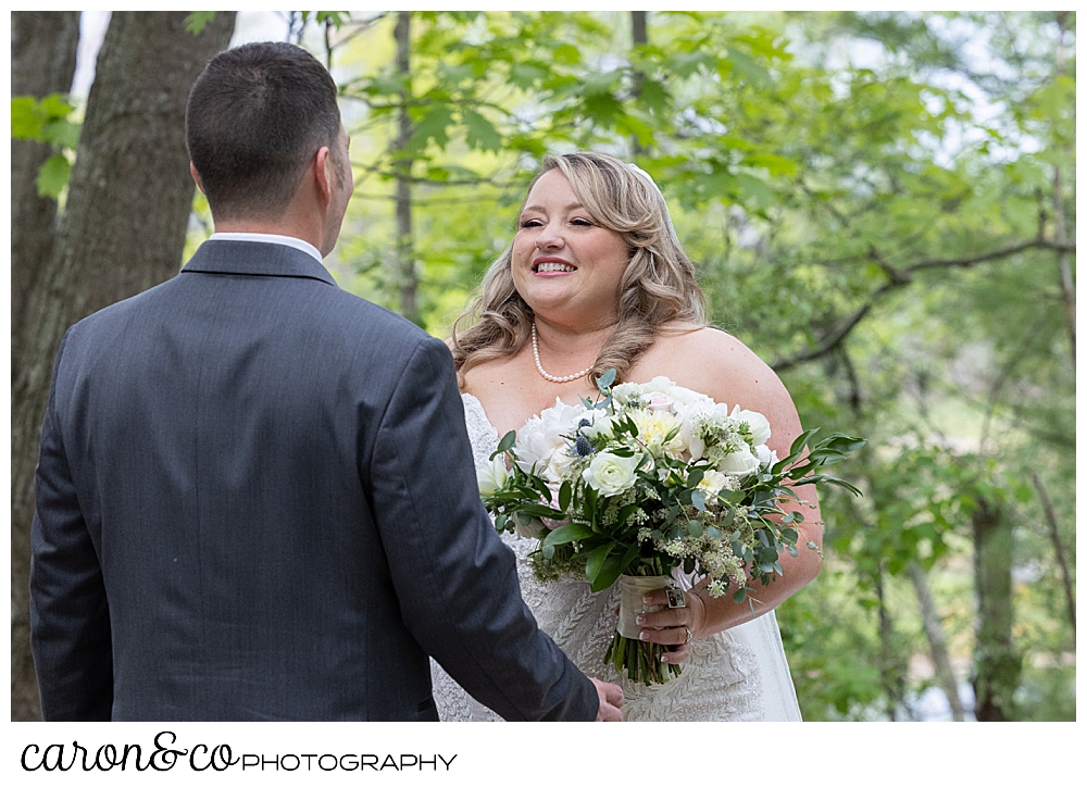 a bride wearing a strapless white dress, holding a bouquet of flowers, smiles as her groom approaches during a wedding day first look