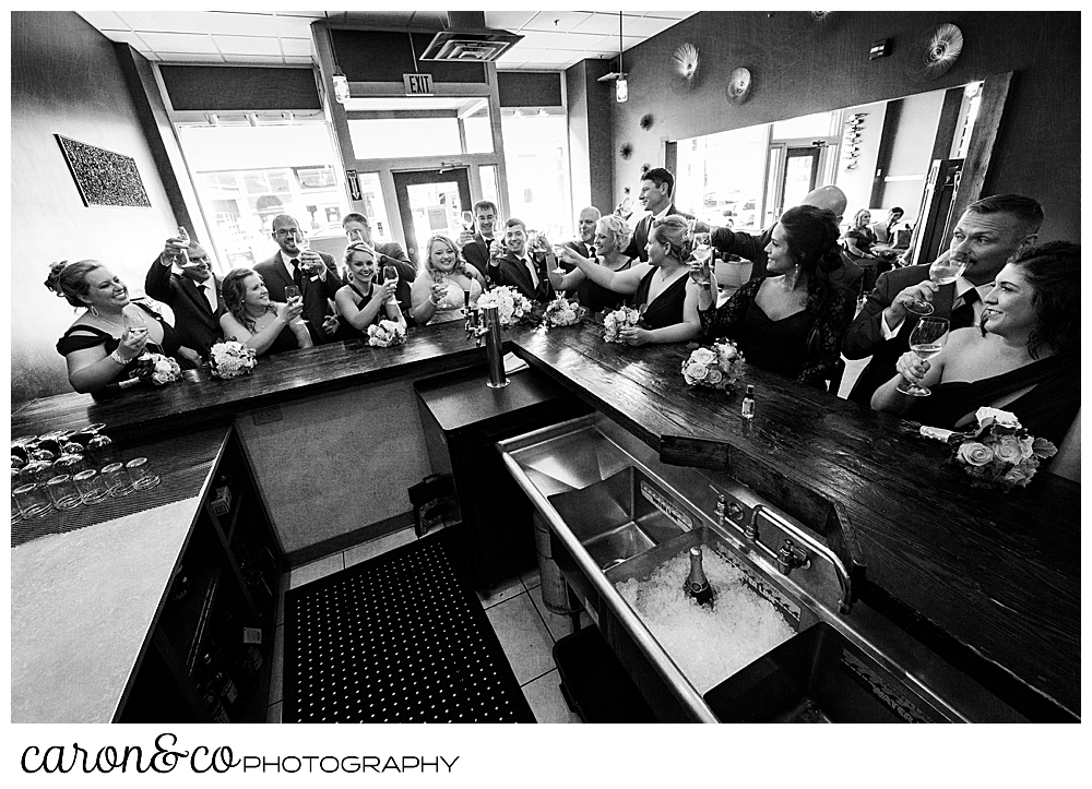 a black and white photo of a bride and groom, with their 16 person bridal party, toasting with Champagne at Sur Lie restaurant in Portland, Maine