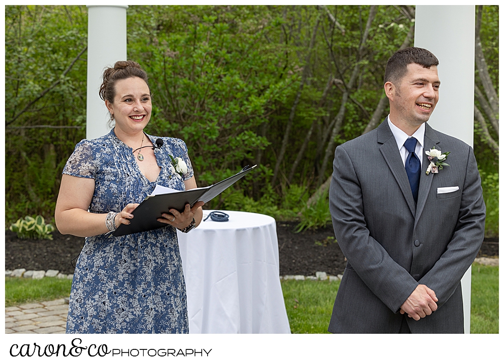 a groom and an officiant stand under the pergola awaiting the bride for a Pine Point Maine wedding ceremony