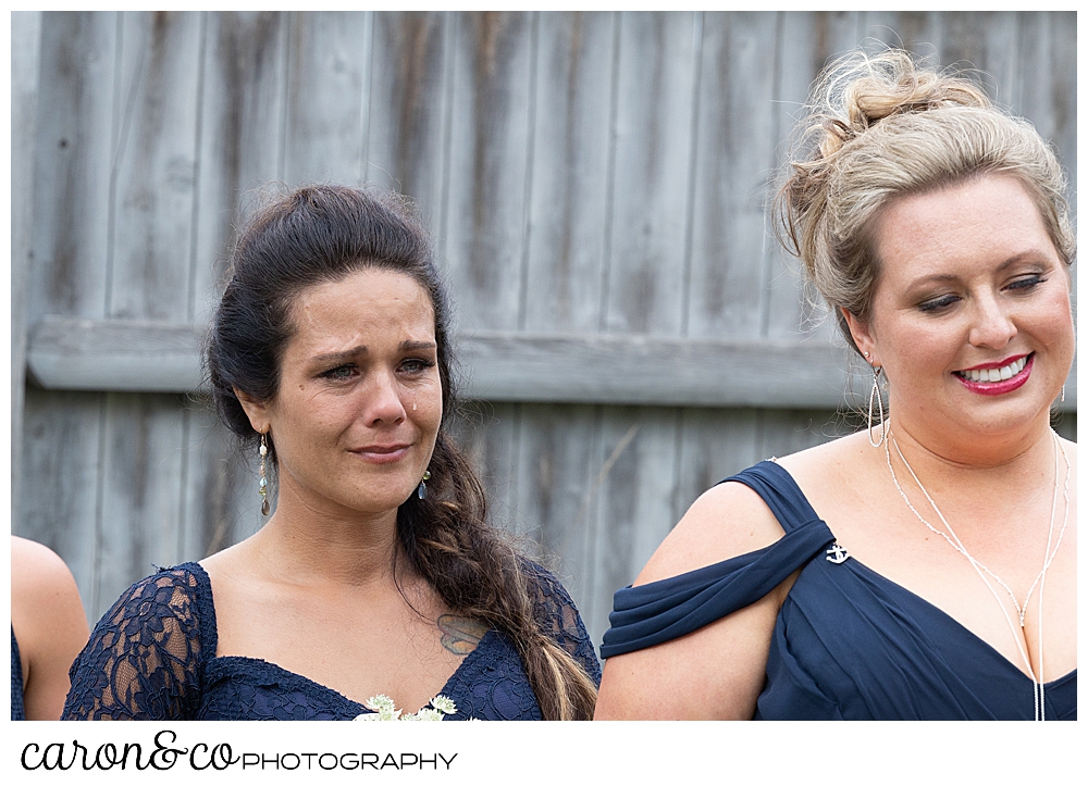 a bridesmaid with dark hair, wearing a blue dress, shows emotion during a Pine Point Maine wedding ceremony