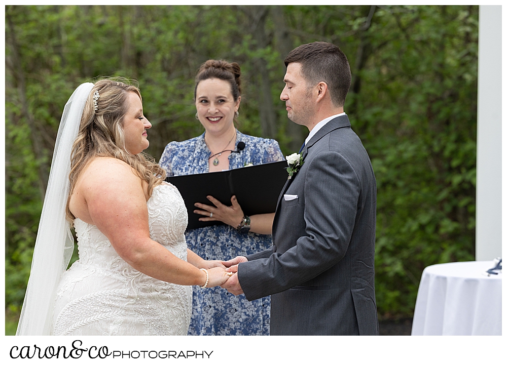 a bride and groom hold hands in front of their officiant, during their wedding ceremony outside at the Landing at Pine Point, Scarborough, Maine