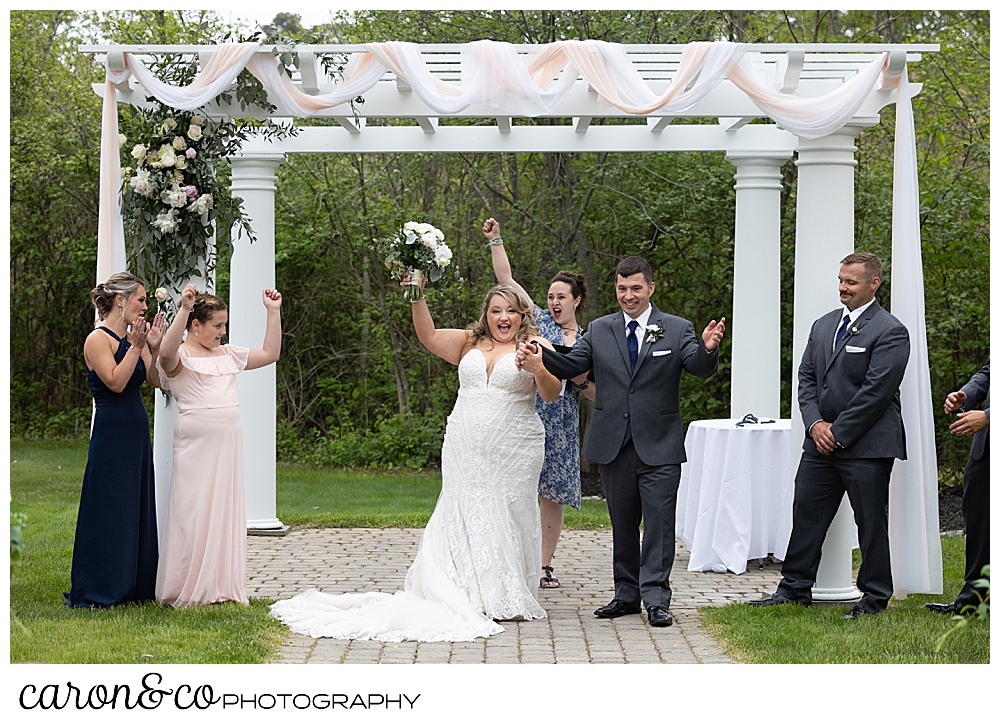 a bride and groom raise their arms to cheer their marriage as they stand in front of the pergola at the Landing at Pine Point, Scarborough, Maine