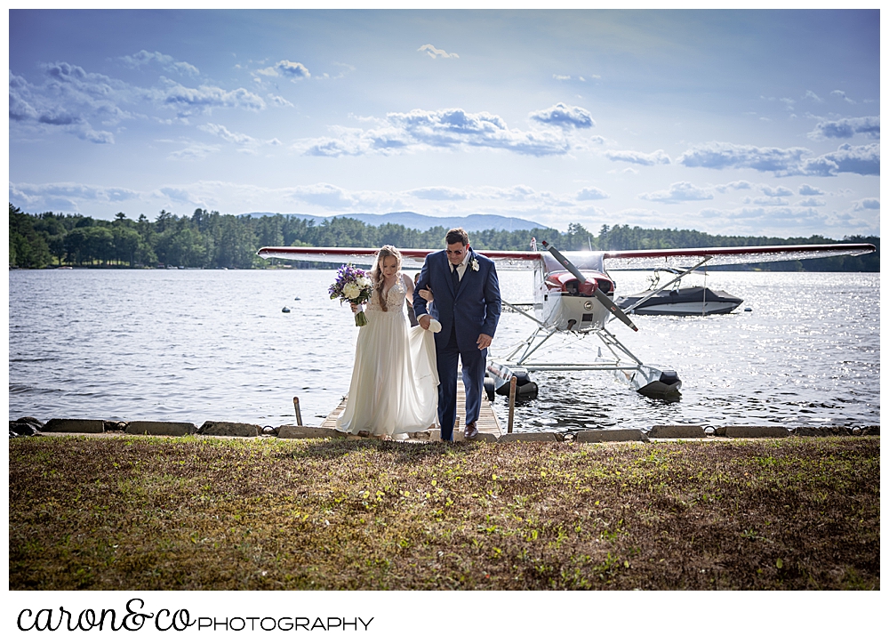 a bride and her dad step out of a sea plane, and begin to walk down the aisle, at a highland lake maine wedding highland lake maine wedding