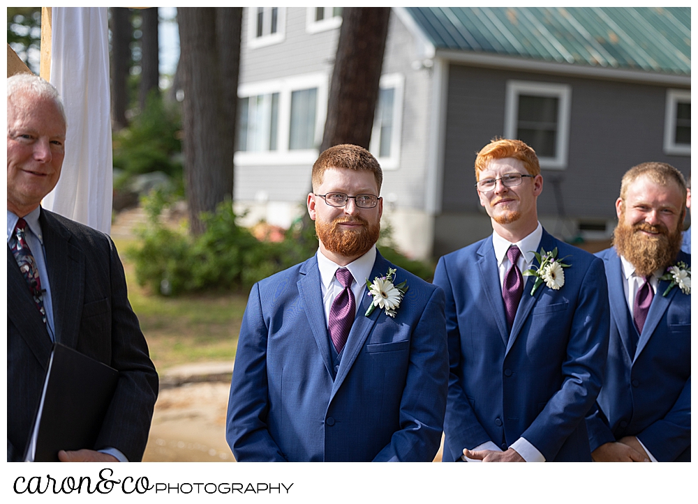 an officiant, dressed in black; and a groom, and best man dressed in blue, await the bride and her father