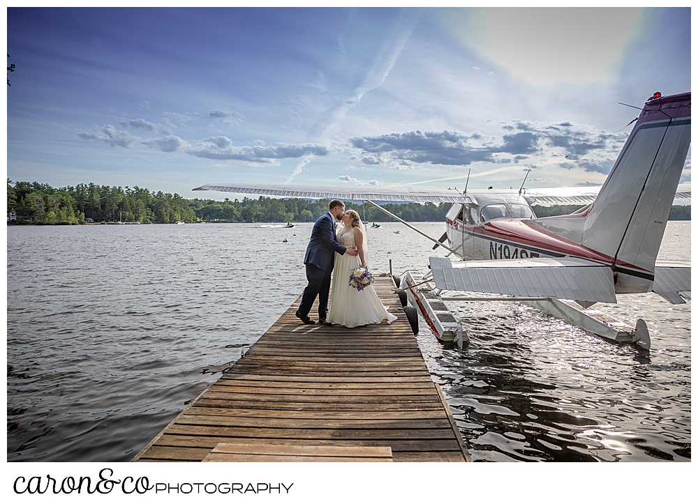 bride and groom kissing on a dock, with a sea plane in the background, at their highland lake maine wedding