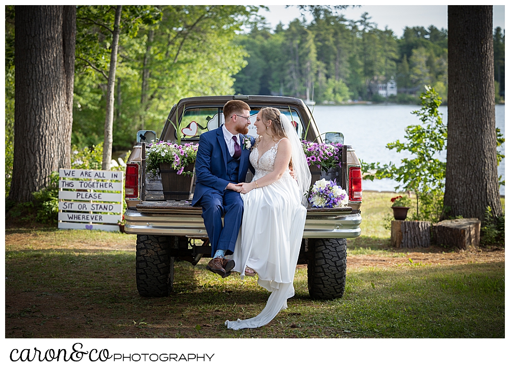 a bride and groom sit on the tailgate of a vintage truck at their highland lake maine wedding