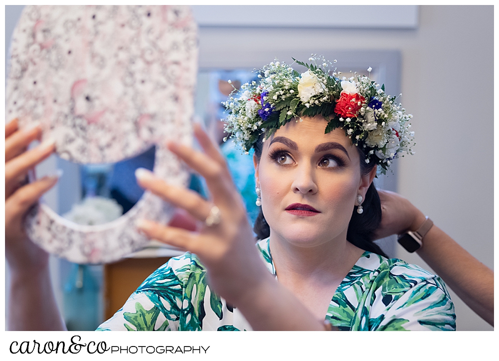 a bride holds a mirror, while she checks her flowered headpiece