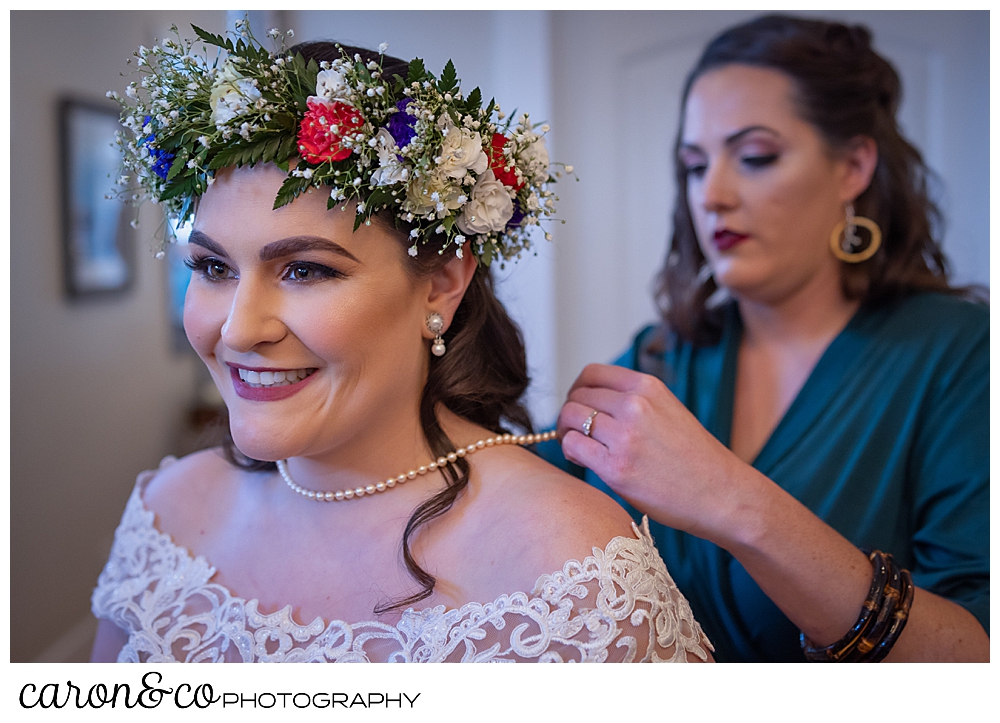 a bridesmaid helps a bride put on a string of pearls