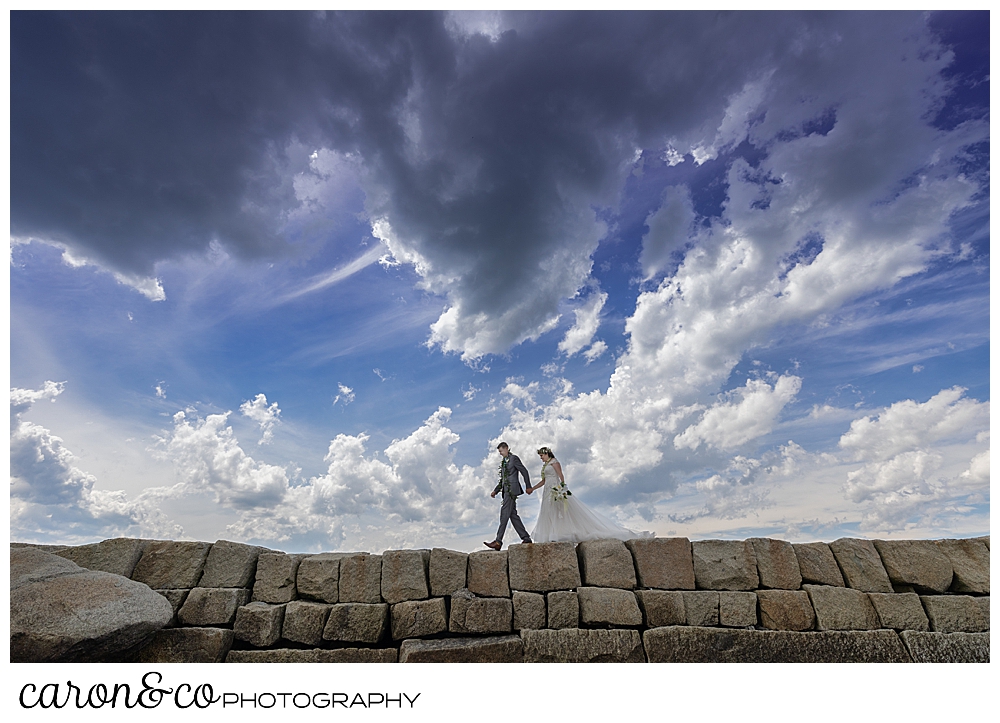 a bride and groom walk hand in hand along the Kennebunkport Breakwater, Kennebunkport, Maine