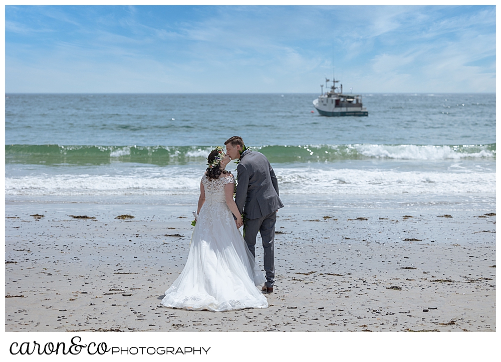 a bride and groom kiss, their backs to the camera, as they stroll on Colony Beach, Kennebunkport, Maine