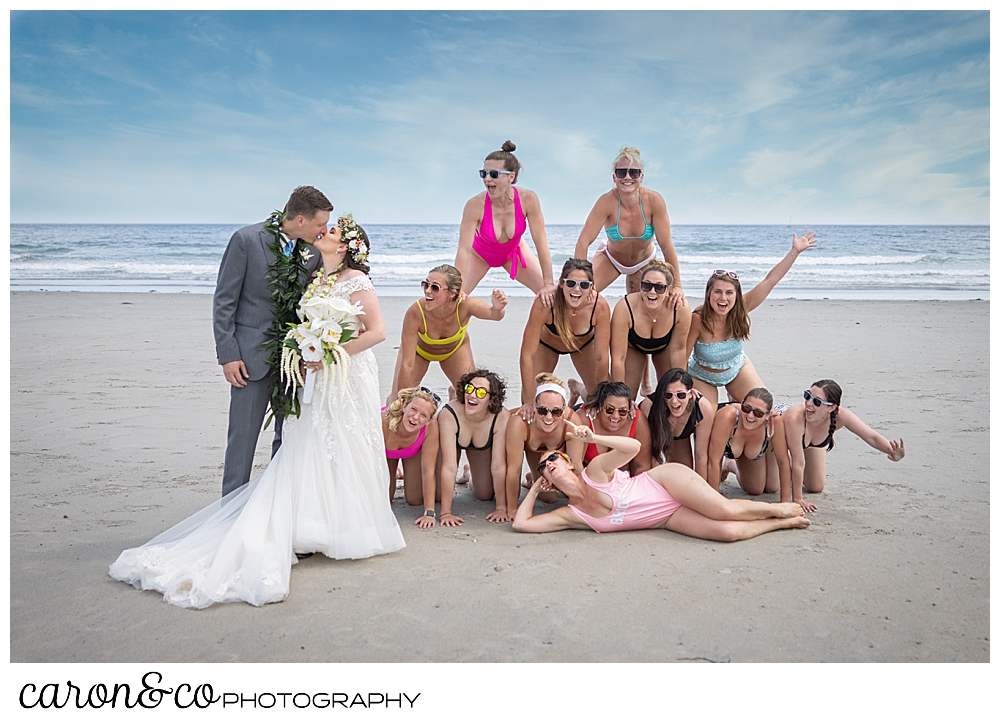 a bride and groom kiss next to a pyramid of bikini clad women, on Gooch's beach, Kennebunk Maine
