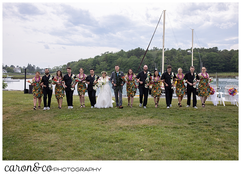 a bride and groom and their bridal party have linked arms and walking across the lawn at the Nonantum Resort, Kennebunkport, Maine