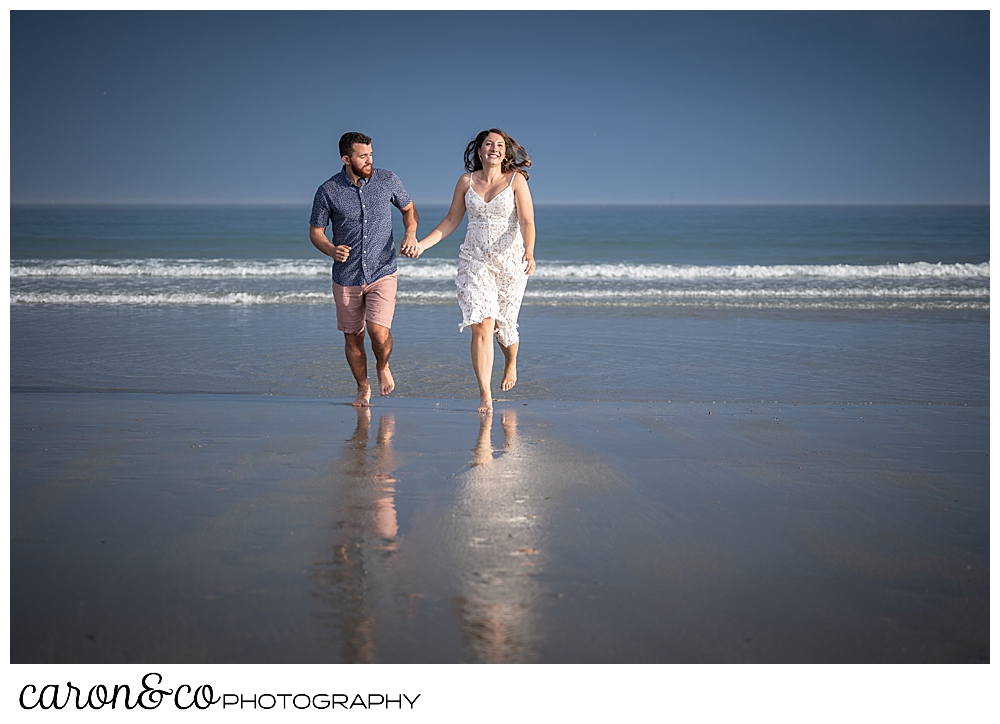 a man and woman run in the surf at Gooch's Beach, during their Kennebunkport engagement session