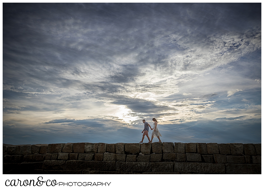 a man and woman walk on the breakwater in Kennebunkport, Maine, during their Kennebunkport engagement session