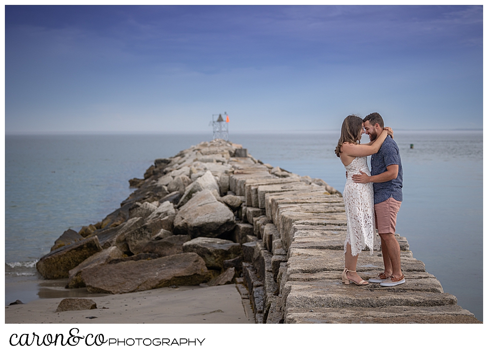 a man and woman stand together with their foreheads together on the Kennebunkport Maine breakwater, during their Kennebunkport engagement session