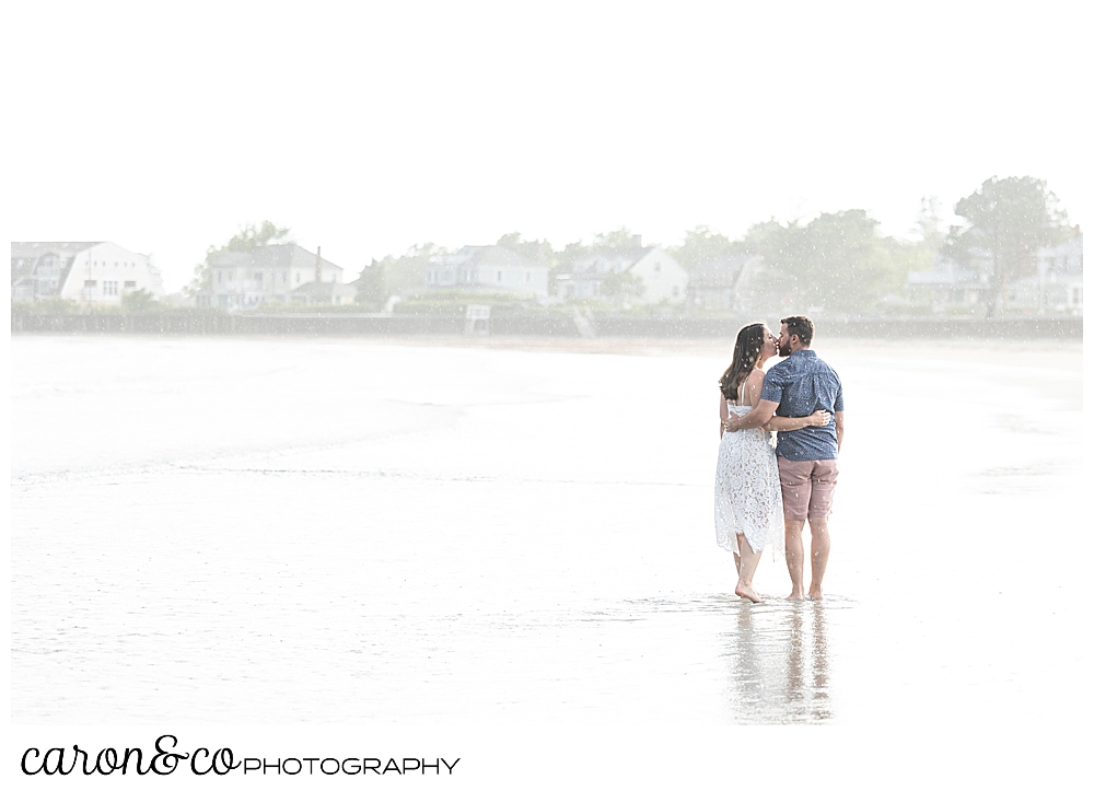 a man and woman, their backs to the camera, kiss each other at Gooch's Beach, Kennebunk, Maine, during their Kennebunkport engagement session