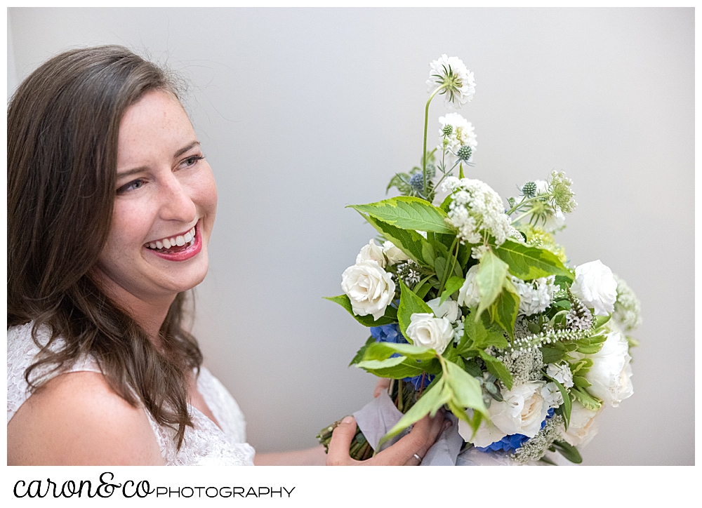 a smiling bride holding a bouquet of white flowers with greens