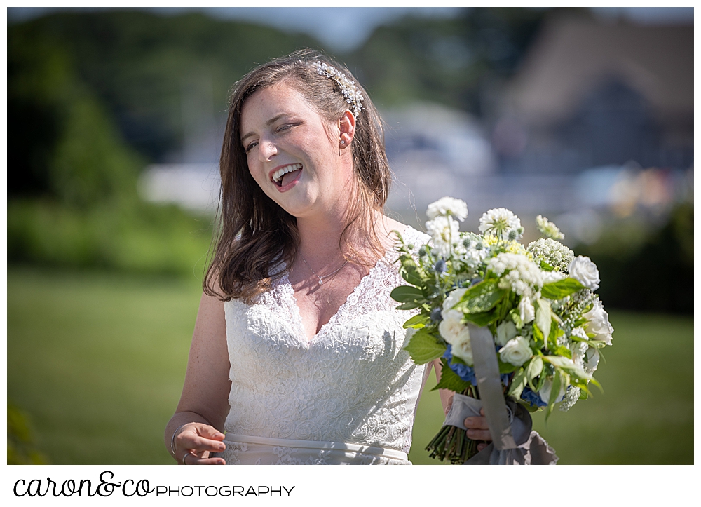 a bride, standing outside on a green lawn, is smiling, and holding a white and green bouquet