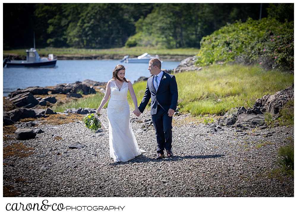 a bride and groom, holding hands as they walk on a beach on the Kennebunk River.