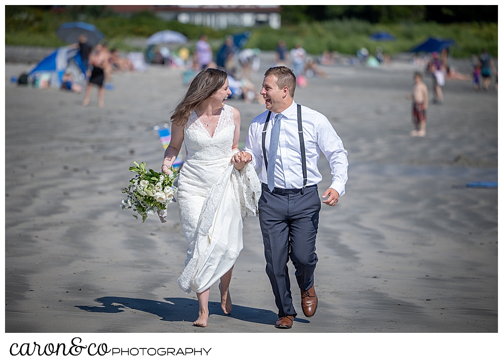 a bride and groom are holding hands, laughing at each other, and running on the beach towards the camera