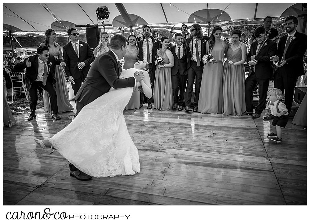 black and white photo of a bride and groom dancing, the groom is dipping the bride, as their bridal party looks on from the edge of the dance floor at a Nonantum Resort wedding celebration