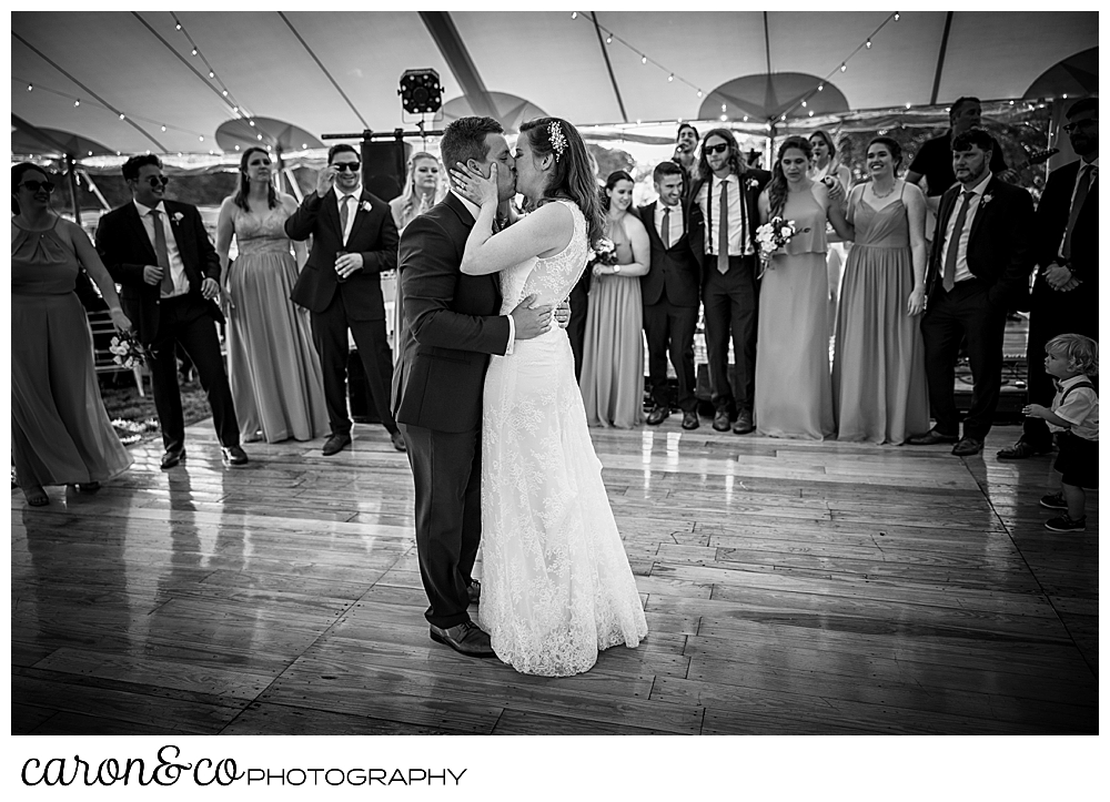 black and white photo of a bride and groom kissing during their dance while their bridal party watches from the side of the dance floor, at a Nonantum Resort wedding celebration