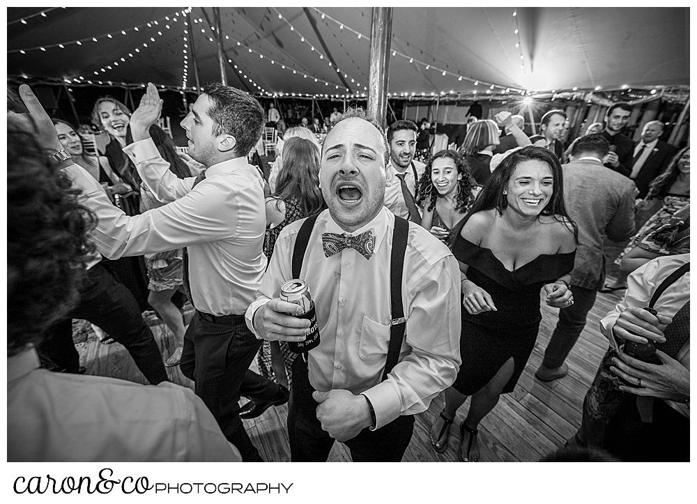 black and white photo of a wedding guests with a beer can, singing while guests around are dancing on the dance floor