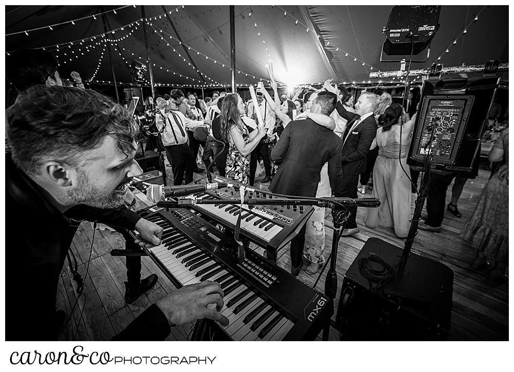 black and white photo of a keyboard player from the band Cover Story Entertainment in the foreground, and guests dancing on the dance floor in the back ground