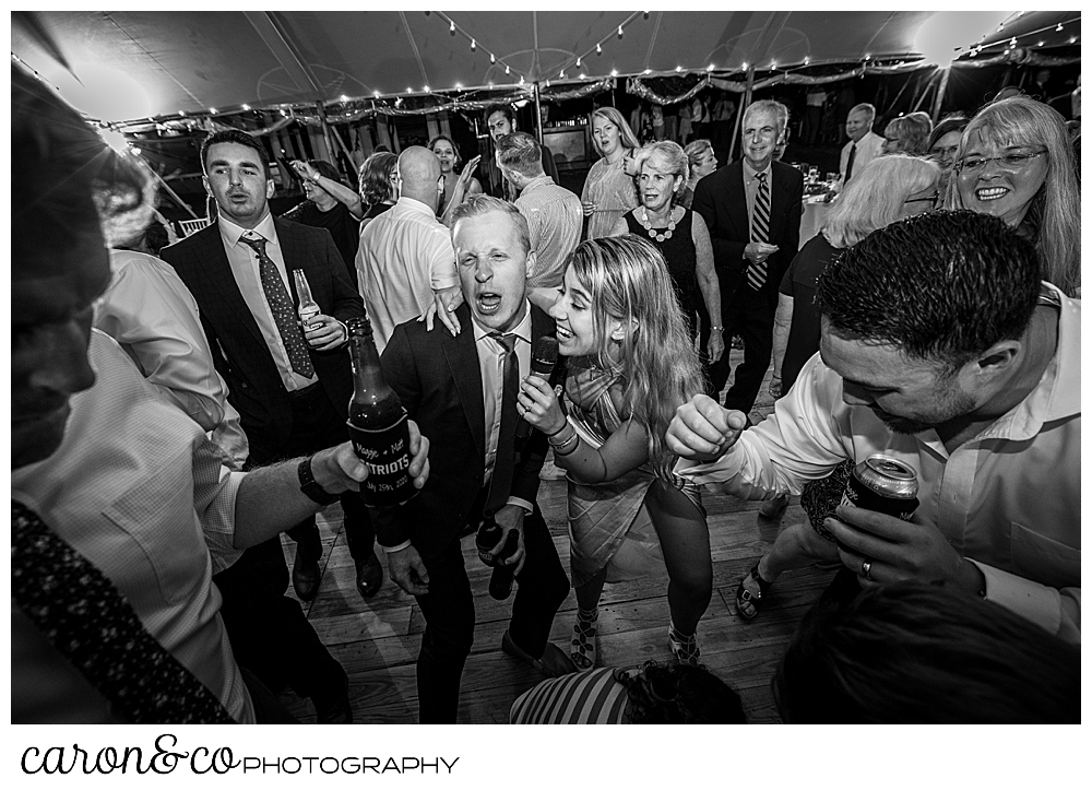 black and white photo of a singer from Cover Story Entertainment, singing with a wedding guest while guests dance at a Nonantum Resort wedding celebration