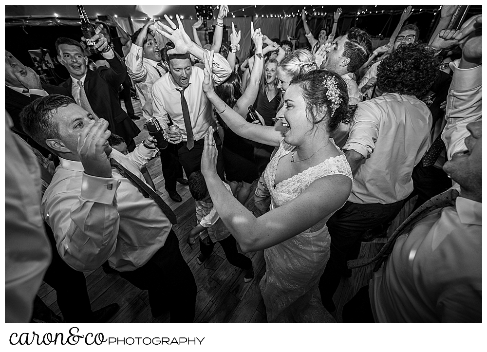 black and white photo of a bride and groom dancing with a packed dance floor, many guests have their hands up in the air