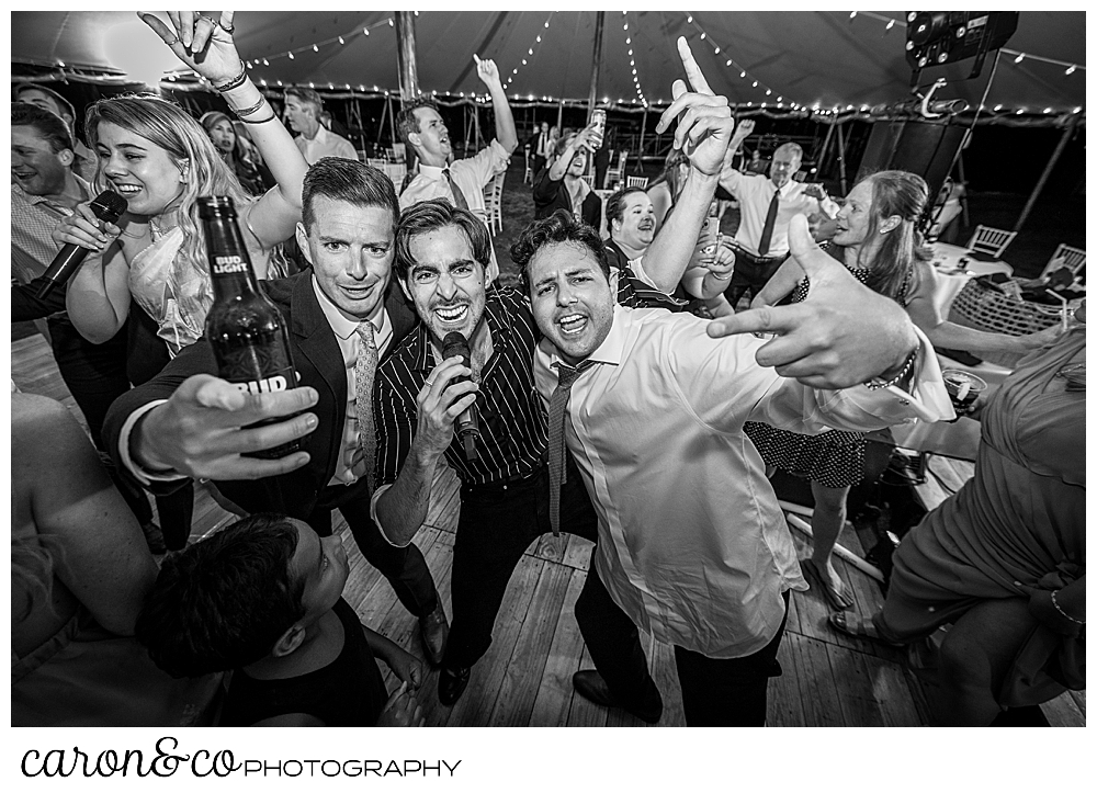 black and white photo of a singer from Cover Story Entertainment sings surrounded by two wedding guests, other guests are dancing in the background