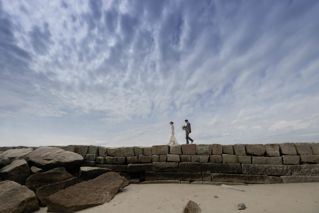 a bride and groom walk along the top of the Kennebunkport Breakwater, Kennebunkport, Maine