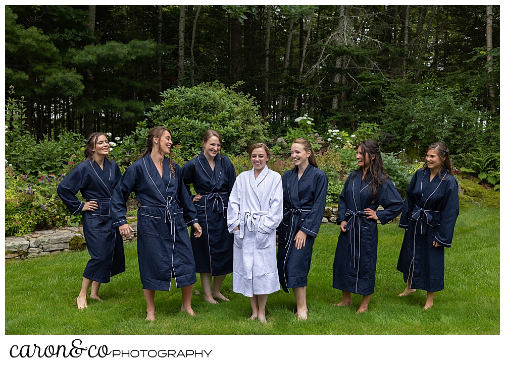 a bride wearing a white robe, and bridesmaids in blue robes, stand together in a woodland garden