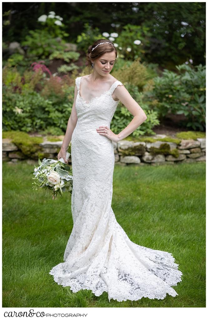 a full length portrait of a bride wearing a sleeveless white dress, and holding a pink, white, and green bouquet, standing in a garden